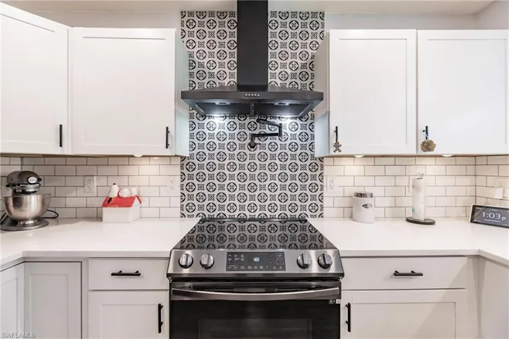 Kitchen featuring tasteful backsplash, wall chimney exhaust hood, stainless steel electric range, and white cabinets