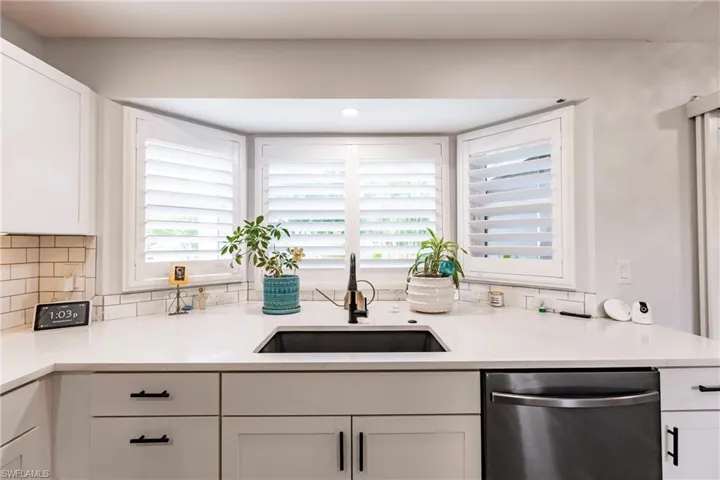Kitchen featuring decorative backsplash, dishwasher, white cabinets, and sink