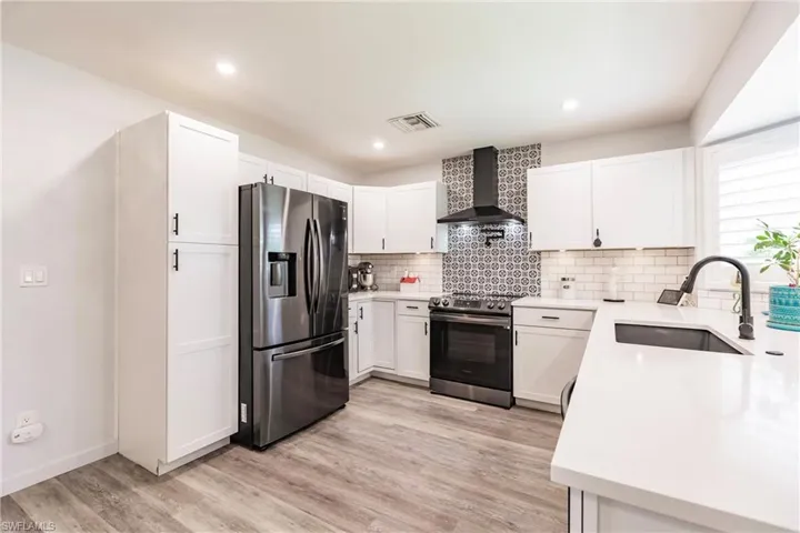 Kitchen with wall chimney exhaust hood, light hardwood / wood-style flooring, stainless steel appliances, sink, and white cabinets