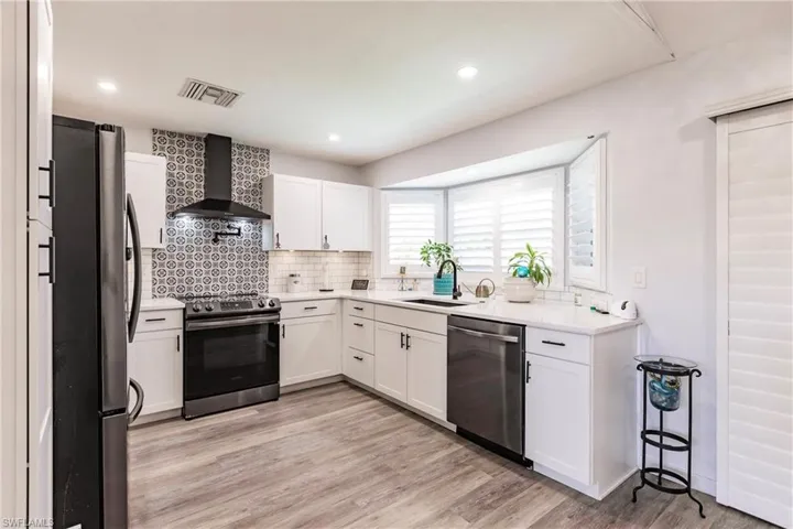 Kitchen with white cabinets, light hardwood / wood-style flooring, sink, wall chimney exhaust hood, and stainless steel appliances
