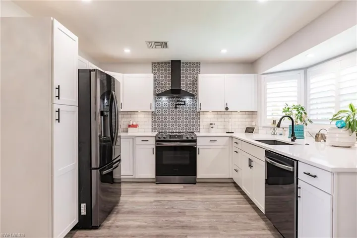 Kitchen with white cabinets, appliances with stainless steel finishes, light hardwood / wood-style floors, wall chimney exhaust hood, and sink