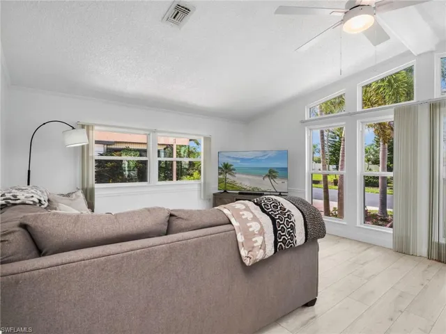 Vaulted ceiling living area featuring light wood-finish flooring, multiple large windows, and a ceiling fan with integrated lighting