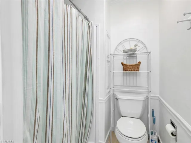 Bathroom featuring a white toilet, white wainscoting, and a shower with a striped curtain
