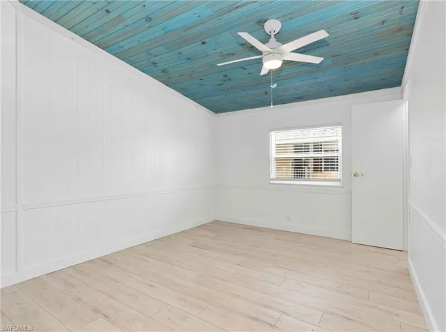 Room featuring a vibrant blue wood-paneled ceiling with a white ceiling fan, light wood-finish flooring, white paneled walls, and a window with horizontal blinds