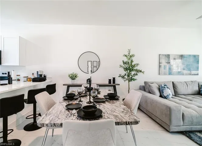 Open concept living area featuring a kitchen island with bar seating, white flat-panel cabinetry, a dining area with a marble-finish table, and tile flooring