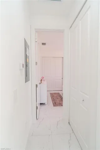 Hallway featuring white walls, white tile flooring with gray veining, and a closet with bifold doors