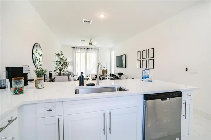 Kitchen island with a stainless steel undermount sink, a gooseneck faucet, white cabinetry, and a built-in stainless steel dishwasher