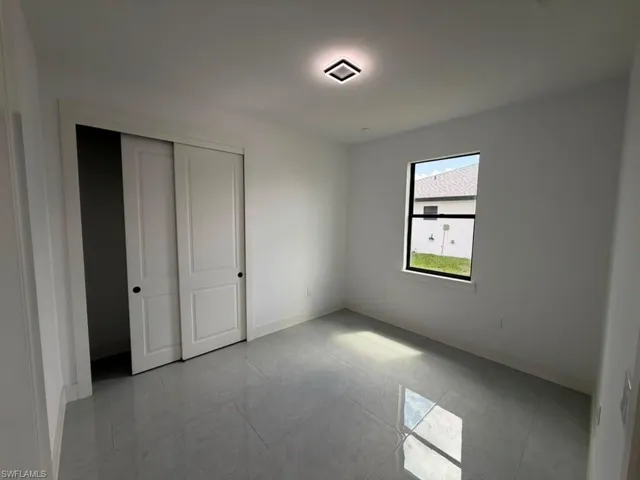 Bright room featuring a single window, a flush-mount ceiling light fixture, and a closet with bi-fold doors, all set on light-toned tile flooring