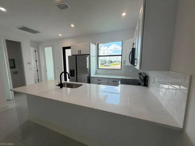 Kitchen featuring a large central island with a sink, white cabinetry, integrated stainless steel appliances, white subway tile backsplash, and recessed lighting