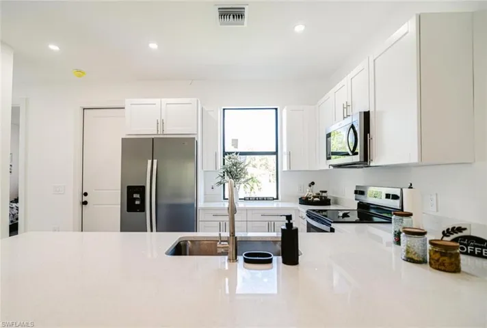Modern kitchen featuring a white countertop island, stainless steel appliances, white cabinetry, and recessed lighting