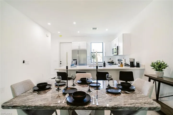 Spacious dining area with a polished stone-finish table, recessed lighting, and bright white walls