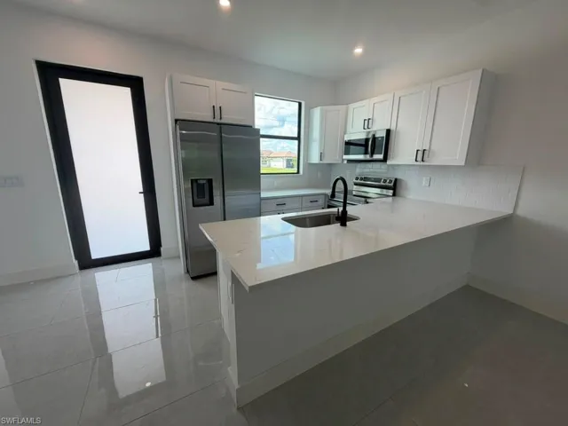 Modern kitchen featuring white shaker cabinetry, stainless steel appliances, a center island with countertop seating, and light-toned tile flooring