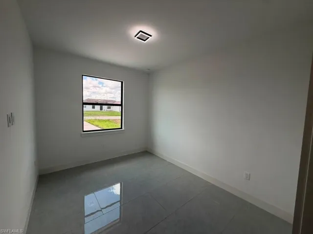 Room with white walls, large window with black trim, square ceiling light fixture, and reflective grey tile flooring