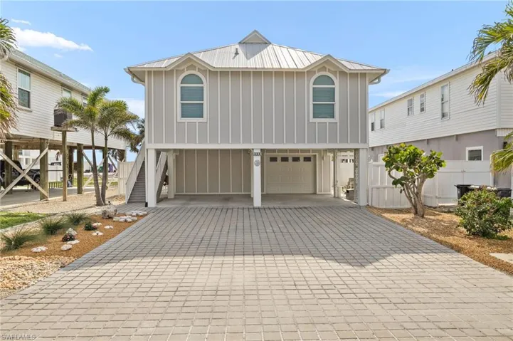 Beach home featuring metal roof, stairway, decorative driveway, a carport, and board and batten siding
