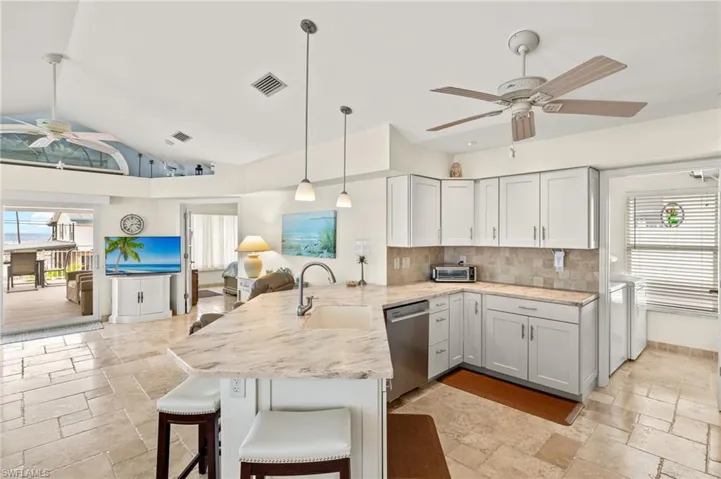 Kitchen featuring a peninsula, a sink, visible vents, stainless steel dishwasher, and stone tile flooring