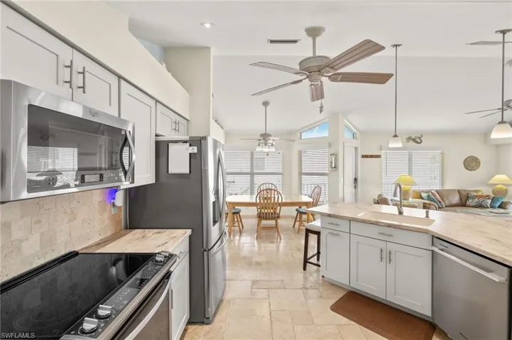 Kitchen featuring stone tile flooring, backsplash, appliances with stainless steel finishes, a ceiling fan, and a sink