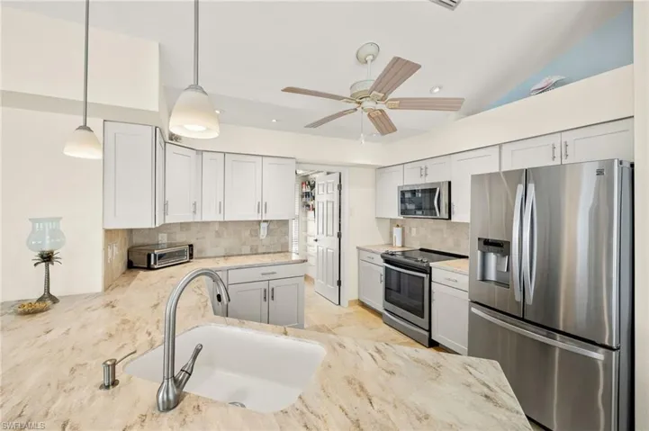 Kitchen featuring stainless steel appliances, a sink, white cabinetry, decorative backsplash, and pendant lighting