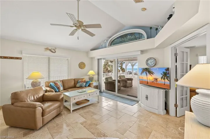 Living room featuring high vaulted ceiling, stone tile flooring, and a ceiling fan