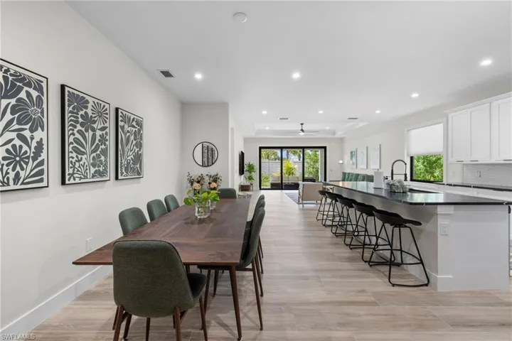 Open-concept living area featuring light wood-finish flooring, recessed lighting, and a contemporary kitchen with white cabinetry and dark countertops