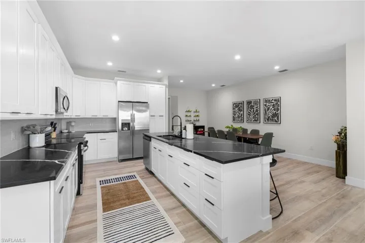 Modern kitchen featuring a large central island with seating, dark countertops, white shaker cabinetry, stainless steel appliances, and wood-finish flooring