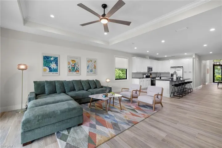 Open-concept interior featuring wood-finish flooring, a tray ceiling with a ceiling fan, recessed lighting, white cabinetry, and a dark kitchen island with seating