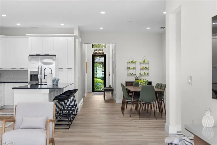Open-concept interior featuring wood-finish flooring, white cabinetry, a kitchen island with seating, recessed lighting, and a prominent entry door with transom window