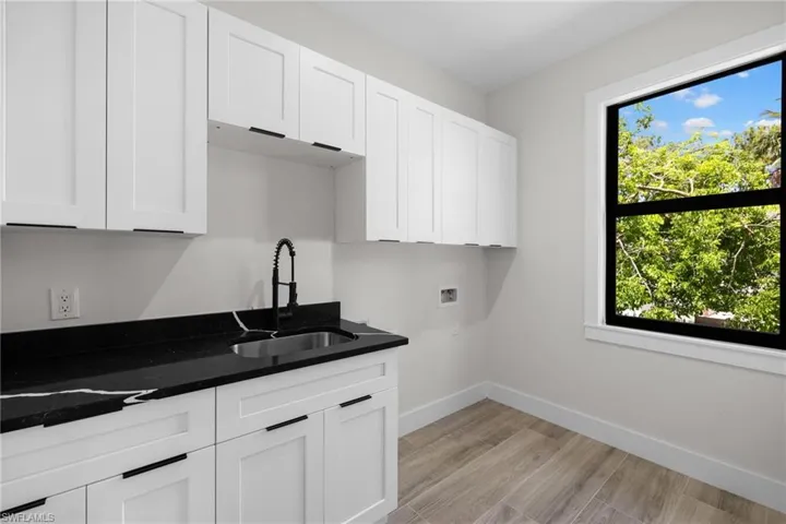 Modern utility room featuring white shaker cabinetry, dark stone countertops with a single basin sink, matte black faucet, and wood-finish tile flooring