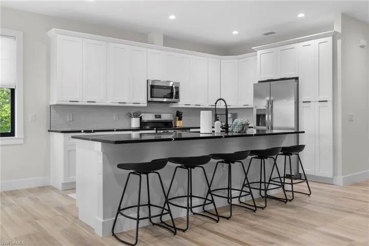 Modern kitchen featuring white shaker-style cabinetry, dark countertops, a large island with seating, stainless steel appliances, and wood-finish flooring