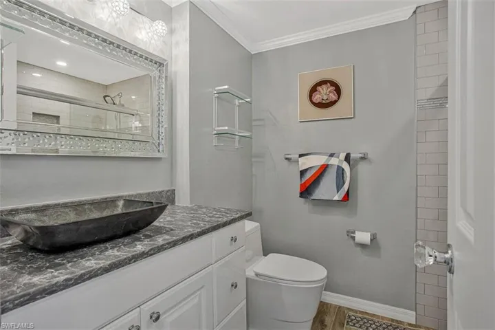 Bathroom with vanity, ornamental molding, a tile shower, and light wood-style flooring