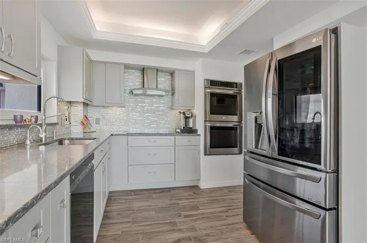 Kitchen featuring stainless steel appliances, a tray ceiling, wood finish floors, and light stone counters