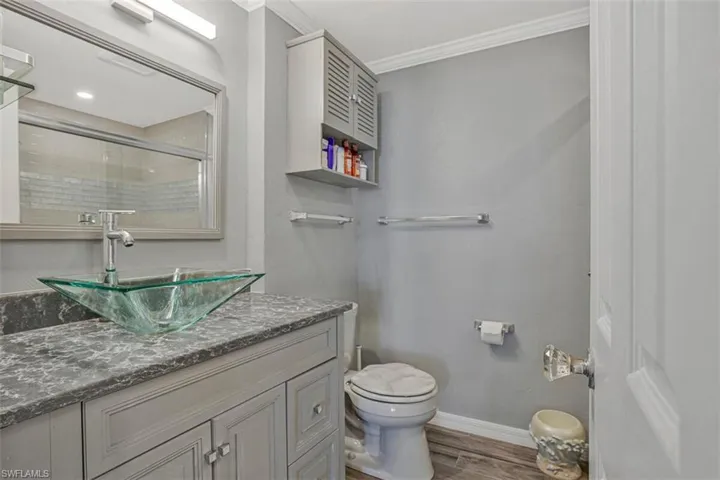 Full bathroom featuring vanity, tiled shower, dark wood-style floors, and ornamental molding