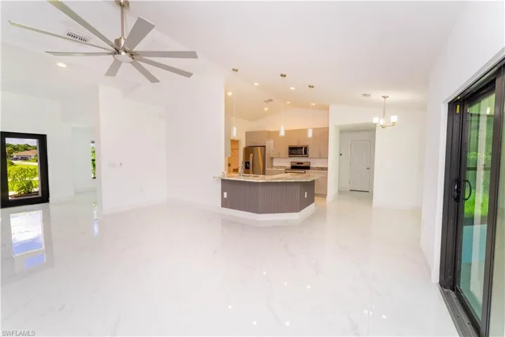 Unfurnished living room featuring vaulted ceiling, a chandelier, ceiling fan, recessed lighting, and light marble finish flooring