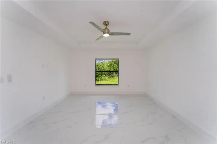 Spare room with a raised ceiling, a ceiling fan, and light marble finish floors