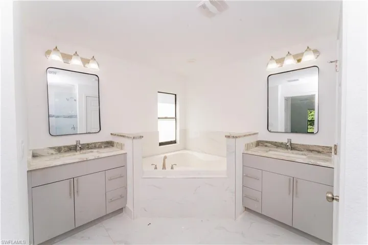 Bathroom with marble finish flooring, two vanities, and a garden tub