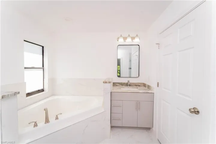 Bathroom with vanity, marble finish floors, and a bath