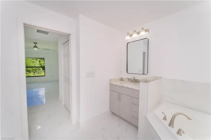 Bathroom featuring vanity, marble finish floors, a garden tub, and ceiling fan