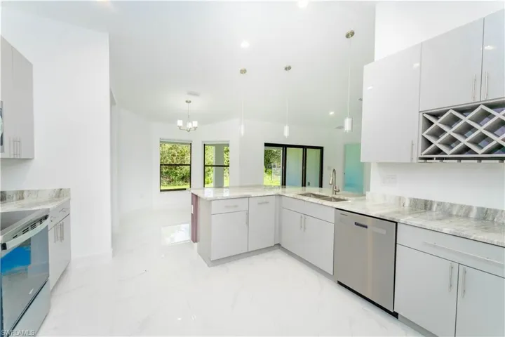 Kitchen with light marble finish flooring, a peninsula, white electric range oven, dishwasher, and a chandelier