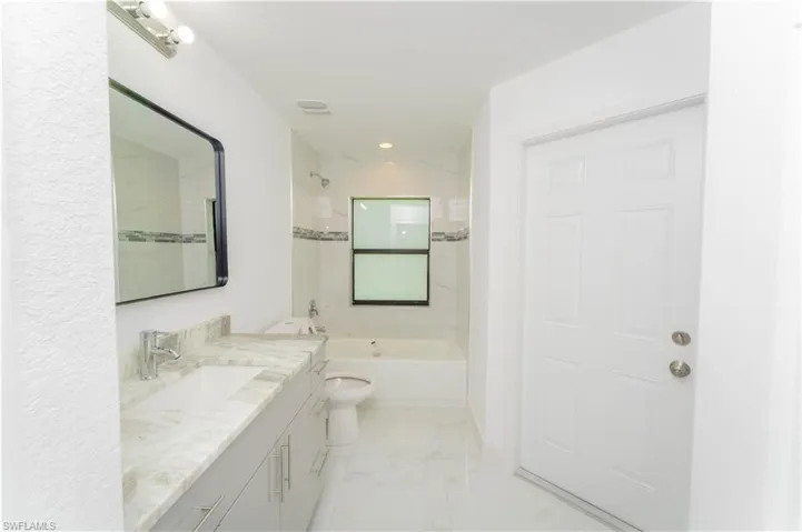 Bathroom with vanity, shower / tub combination, marble look tiles, and recessed lighting