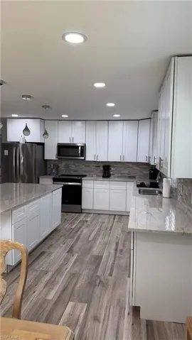 Kitchen featuring stainless steel appliances, a sink, white cabinets, light stone counters, and decorative backsplash