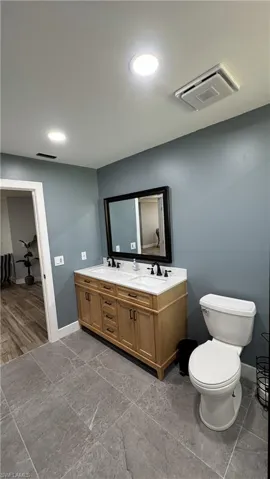 Full bath featuring toilet, double vanity, and baseboards