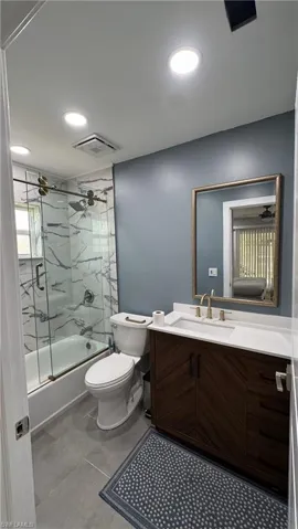 Bathroom featuring enclosed tub / shower combo, toilet, vanity, recessed lighting, and tile patterned flooring