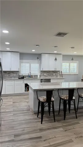 Kitchen featuring backsplash, recessed lighting, white cabinetry, a breakfast bar, and decorative light fixtures