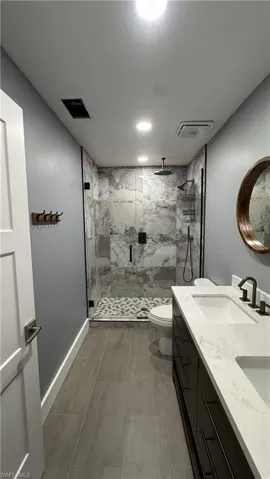 Full bath featuring a marble finish shower, double vanity, toilet, and baseboards