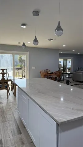 Kitchen featuring white cabinets, light stone counters, decorative light fixtures, and light wood-style flooring