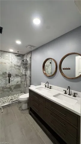 Full bath with a marble finish shower, double vanity, toilet, and recessed lighting