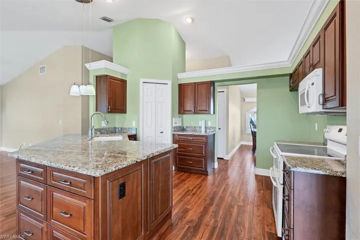 Kitchen with dark hardwood / wood-style flooring, pendant lighting, sink, vaulted ceiling, and white appliances