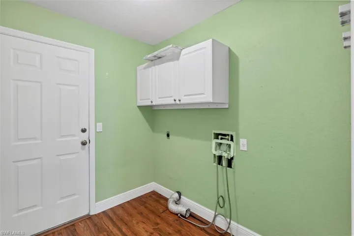 Clothes washing area with dark wood-type flooring, cabinets, hookup for a washing machine, and hookup for an electric dryer
