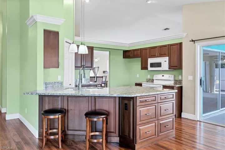 Kitchen with crown molding, kitchen peninsula, dark hardwood / wood-style flooring, and white appliances