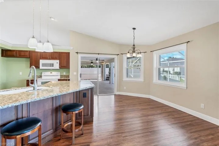 Kitchen with a wealth of natural light, light stone counters, dark hardwood / wood-style floors, and white appliances
