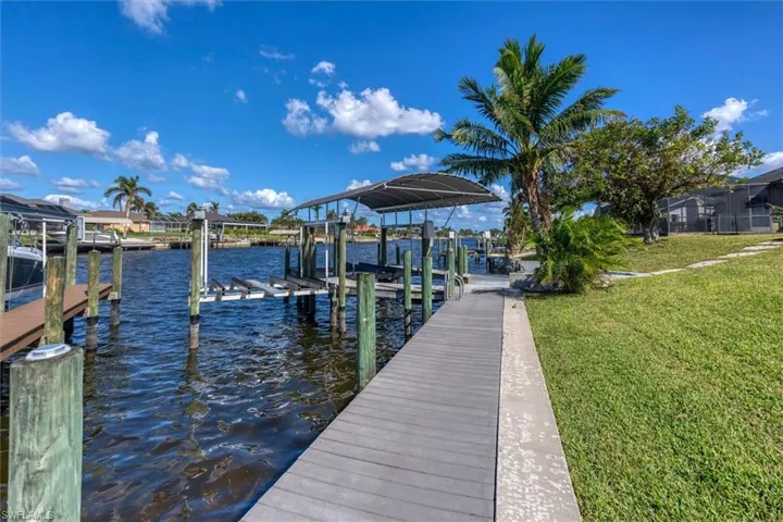 View of dock featuring glass enclosure, a water view, and a lawn